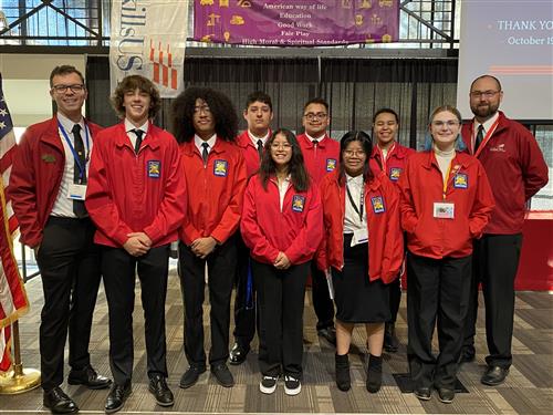 8 GISH students smiling wearing their SkillsUSA red blazers and standing with two teachers